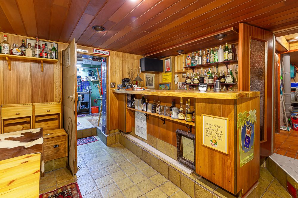 Gemütliche Kellerbar mit Holzverkleidung, Regalen und verschiedenen Flaschen im Regal.
