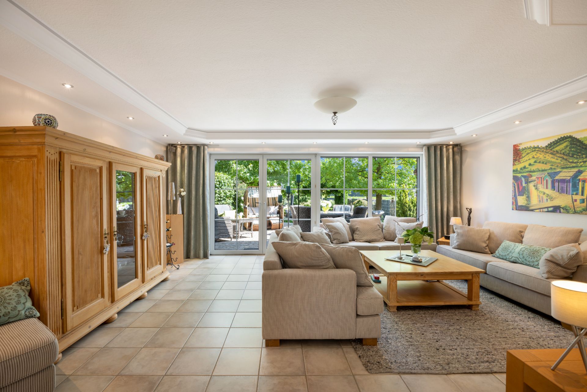 Helles Wohnzimmer mit Sofas, Couchtisch, großem Schrank und Blick auf eine Terrasse mit Garten.