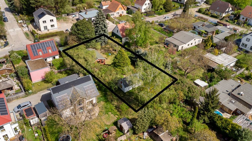 Luftaufnahme eines Grundstücks mit Bäumen und kleinem Haus, schwarz umrandet in Wohngegend.