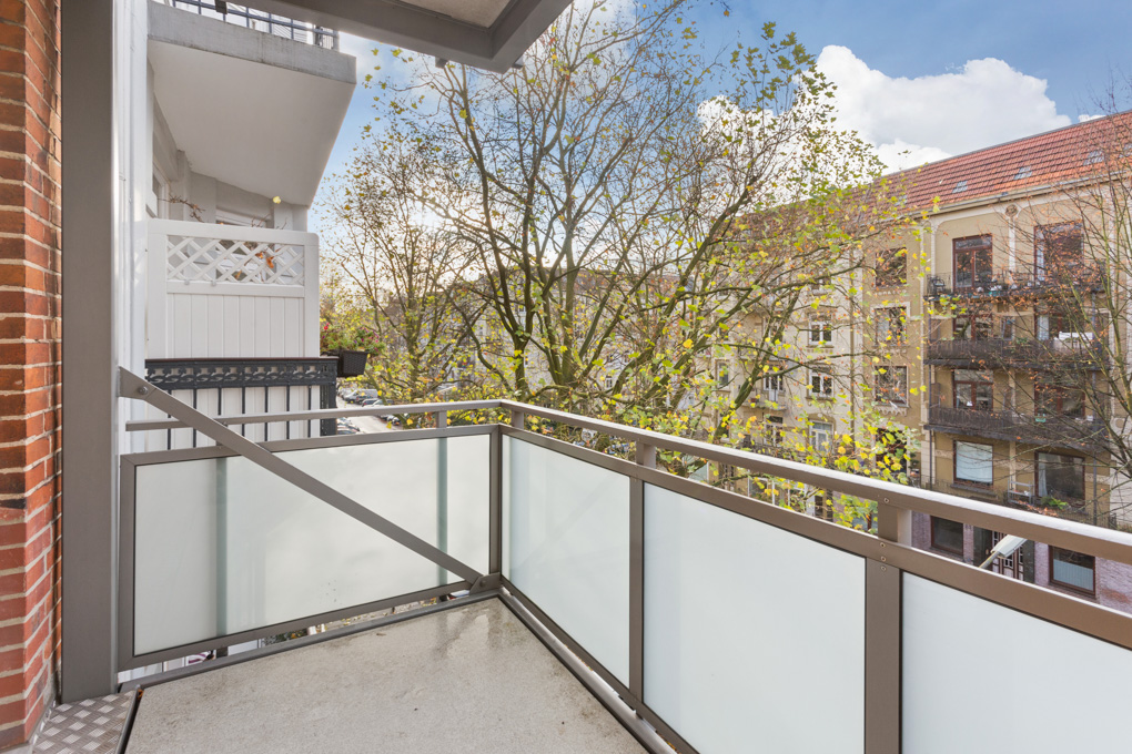 Moderner Balkon mit Glasgeländer, Blick auf Bäume und Nachbargebäude.