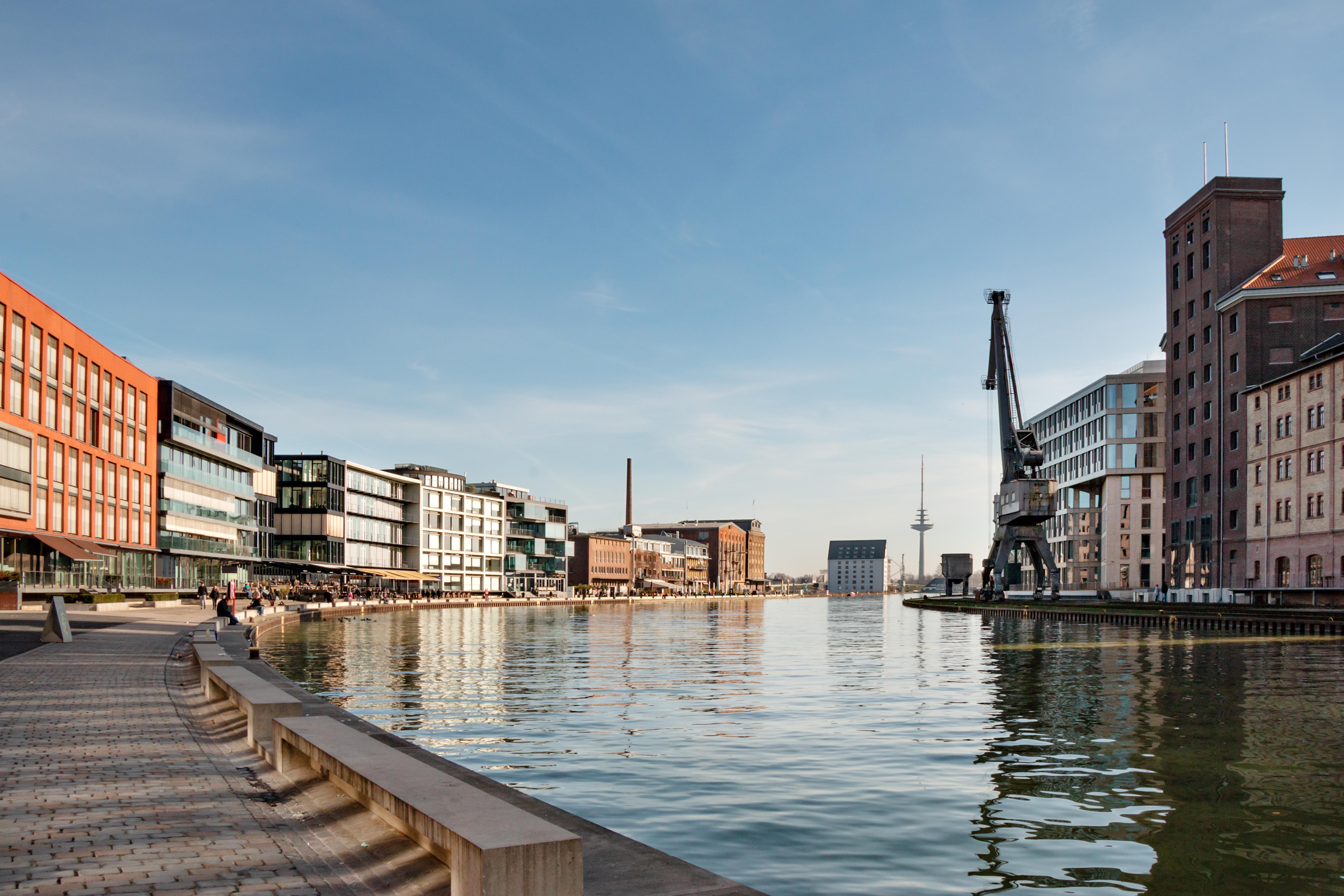 Moderne Wohngebäude und ein Kran an einem breiten Kanal bei sonnigem Wetter.