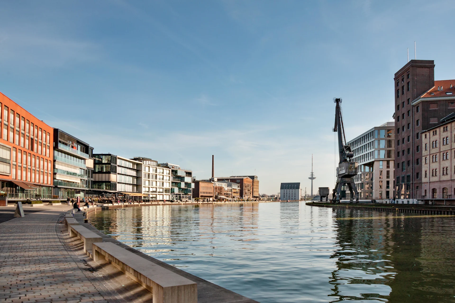 Moderne Wohngebäude und ein Kran an einem breiten Kanal bei sonnigem Wetter.