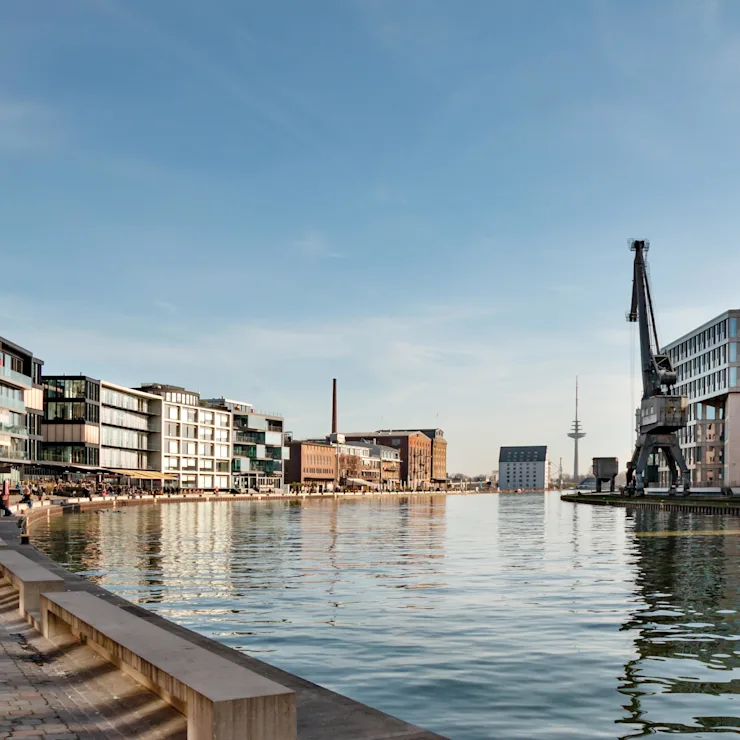 Moderne Wohngebäude und ein Kran an einem breiten Kanal bei sonnigem Wetter.