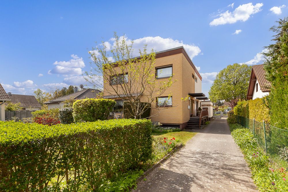 Zweistöckiges Wohnhaus mit Flachdach und Garten, Weg führt am Haus vorbei.