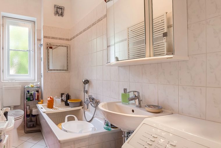Helles Badezimmer mit Badewanne, Waschbecken, Toilette, Waschmaschine und Spiegelschrank.