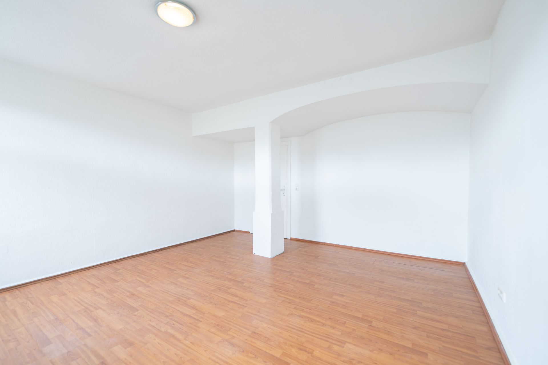 Leerer, heller Raum mit weiß gestrichenen Wänden und Laminatboden.