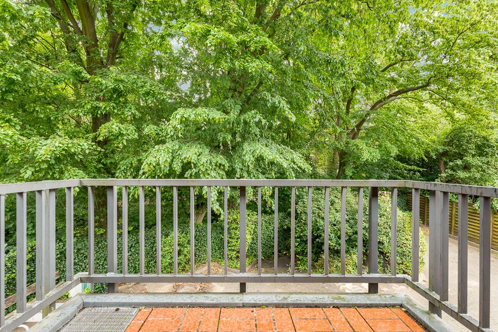 Ein Balkon mit Holzgeländer und Blick auf viele grüne Bäume und Sträucher.