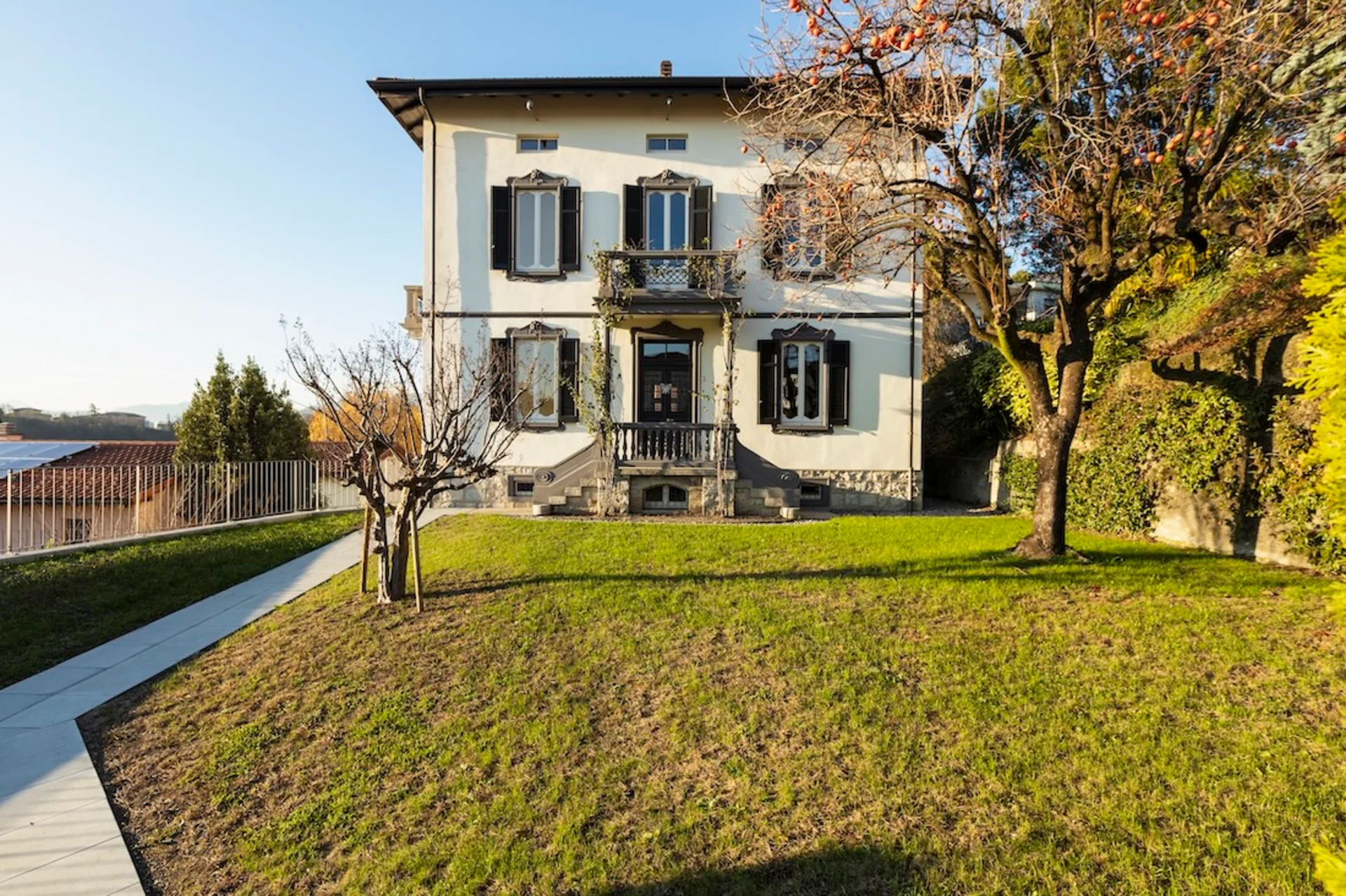 Wohnhaus mit zwei Etagen, Balkon, Garten und Bäumen im Vordergrund.