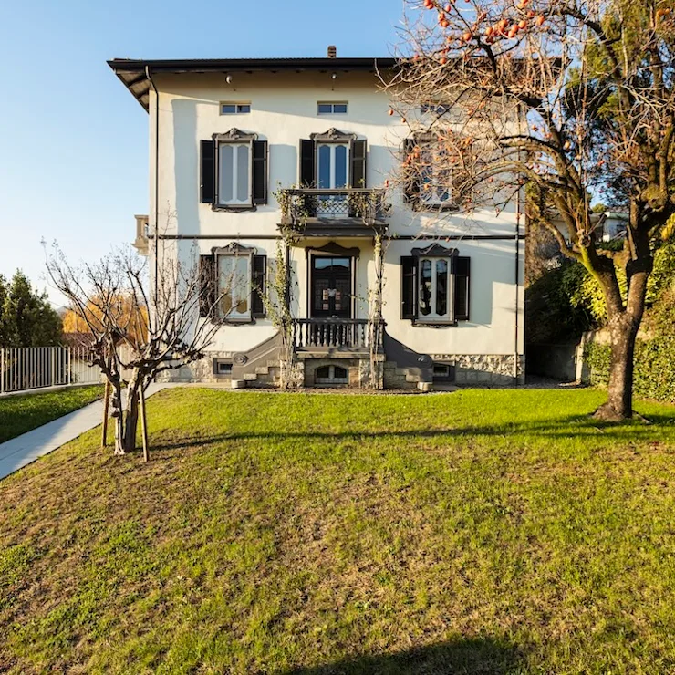 Wohnhaus mit zwei Etagen, Balkon, Garten und Bäumen im Vordergrund.