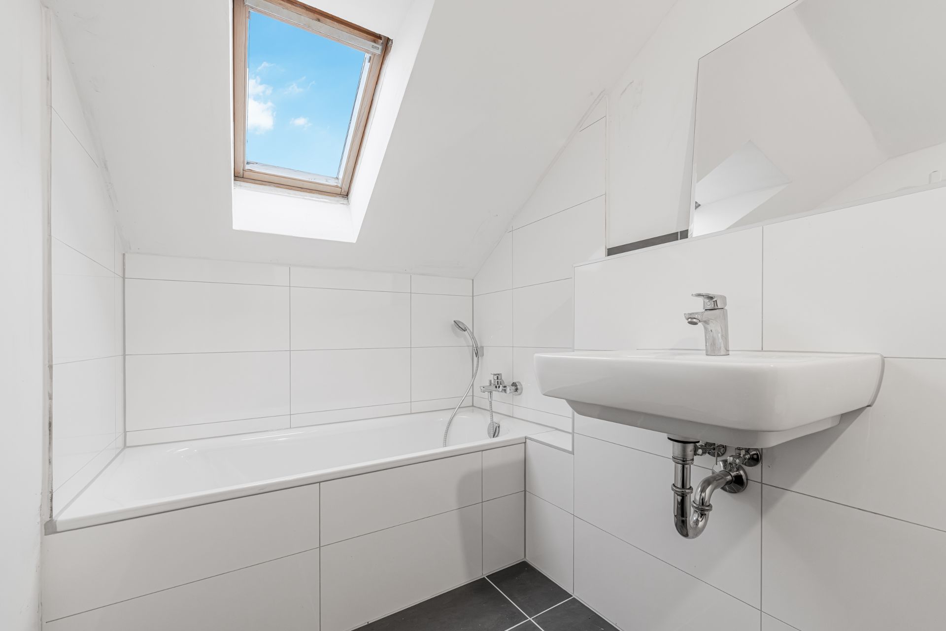 Helles Bad mit Badewanne, Waschbecken und Dachfenster unter einer Schräge.