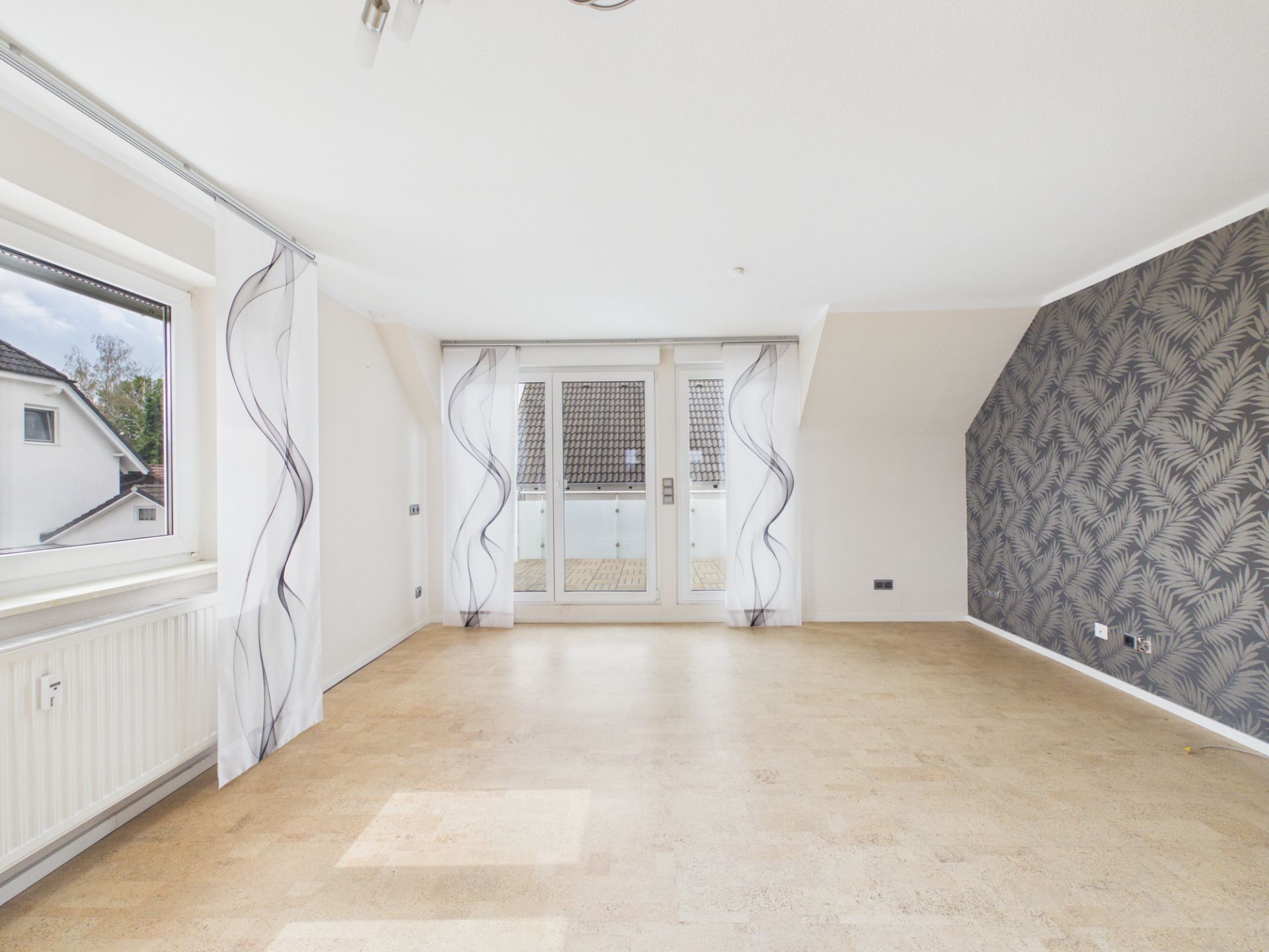Helles, leeres Wohnzimmer mit großen Fenstern, Glastür und gemusterter Tapete an einer Wand.