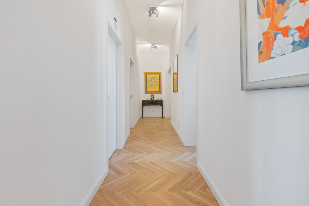 Heller Flur mit Parkettboden, weißen Wänden und mehreren Türen, Bilder an den Wänden.