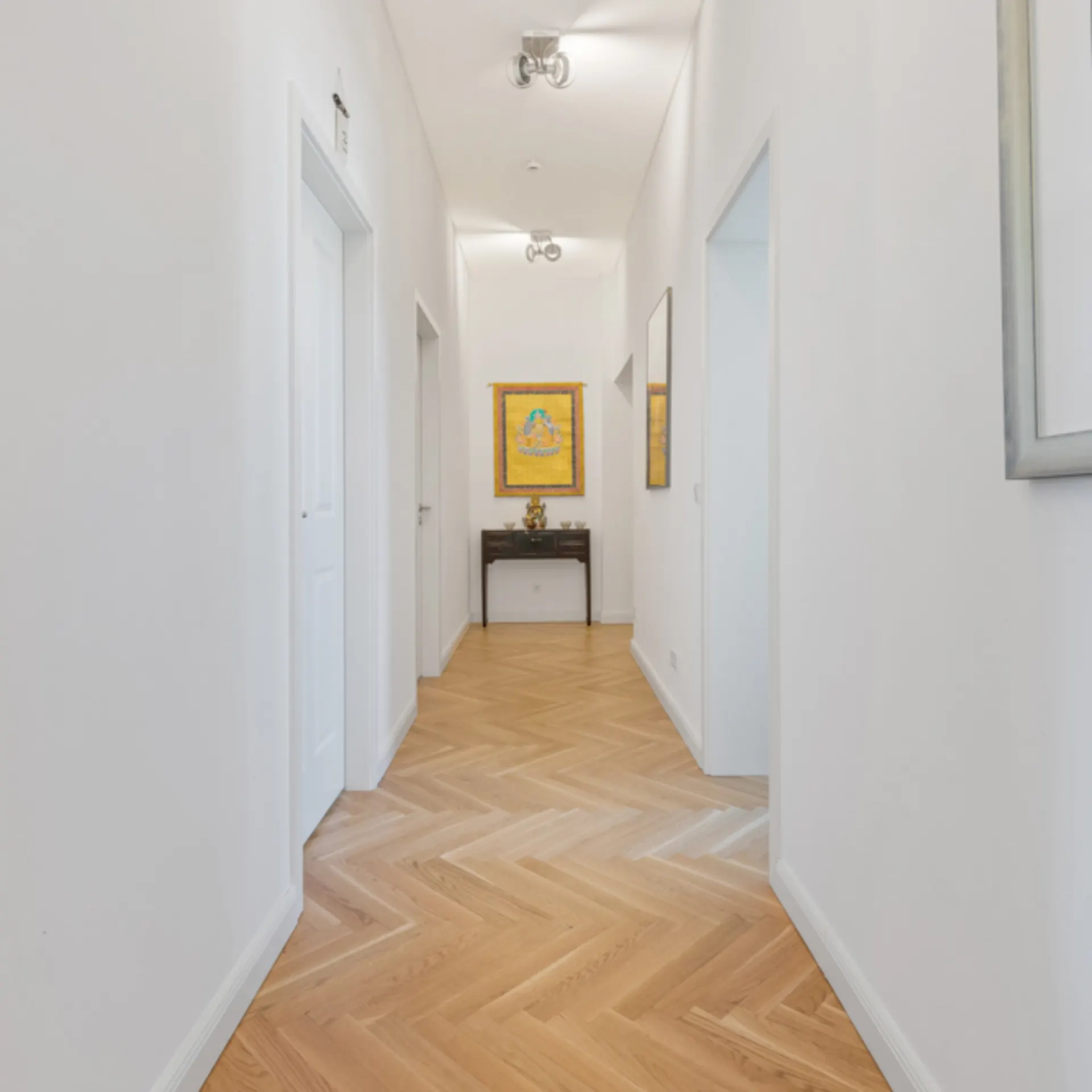 Heller Flur mit Parkettboden, weißen Wänden und mehreren Türen, Bilder an den Wänden.