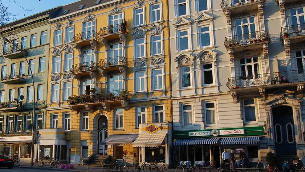 Mehrstöckiges Wohnhaus mit verzierten Fassaden, Balkonen und Geschäften im Erdgeschoss.