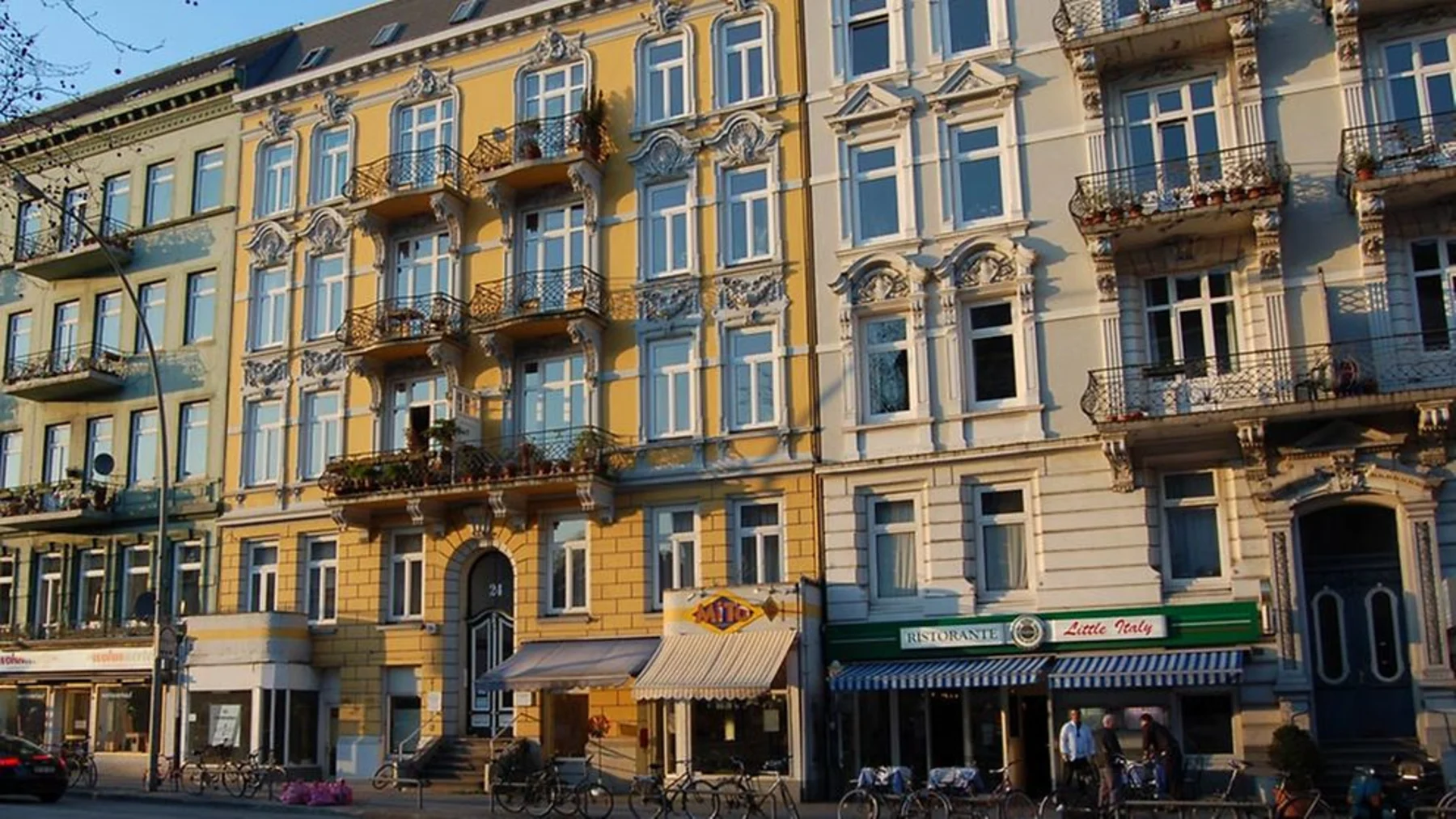 Mehrstöckiges Wohnhaus mit verzierten Fassaden, Balkonen und Geschäften im Erdgeschoss.