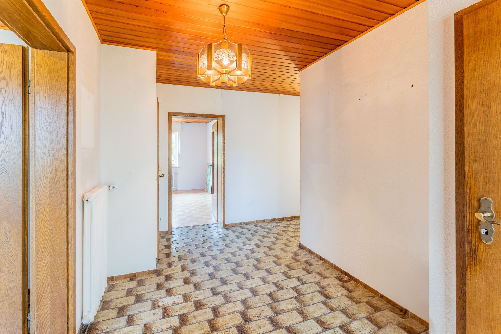Heller Flur mit gemustertem Fliesenboden, Holzdecke und offener Tür zu weiterem Raum.