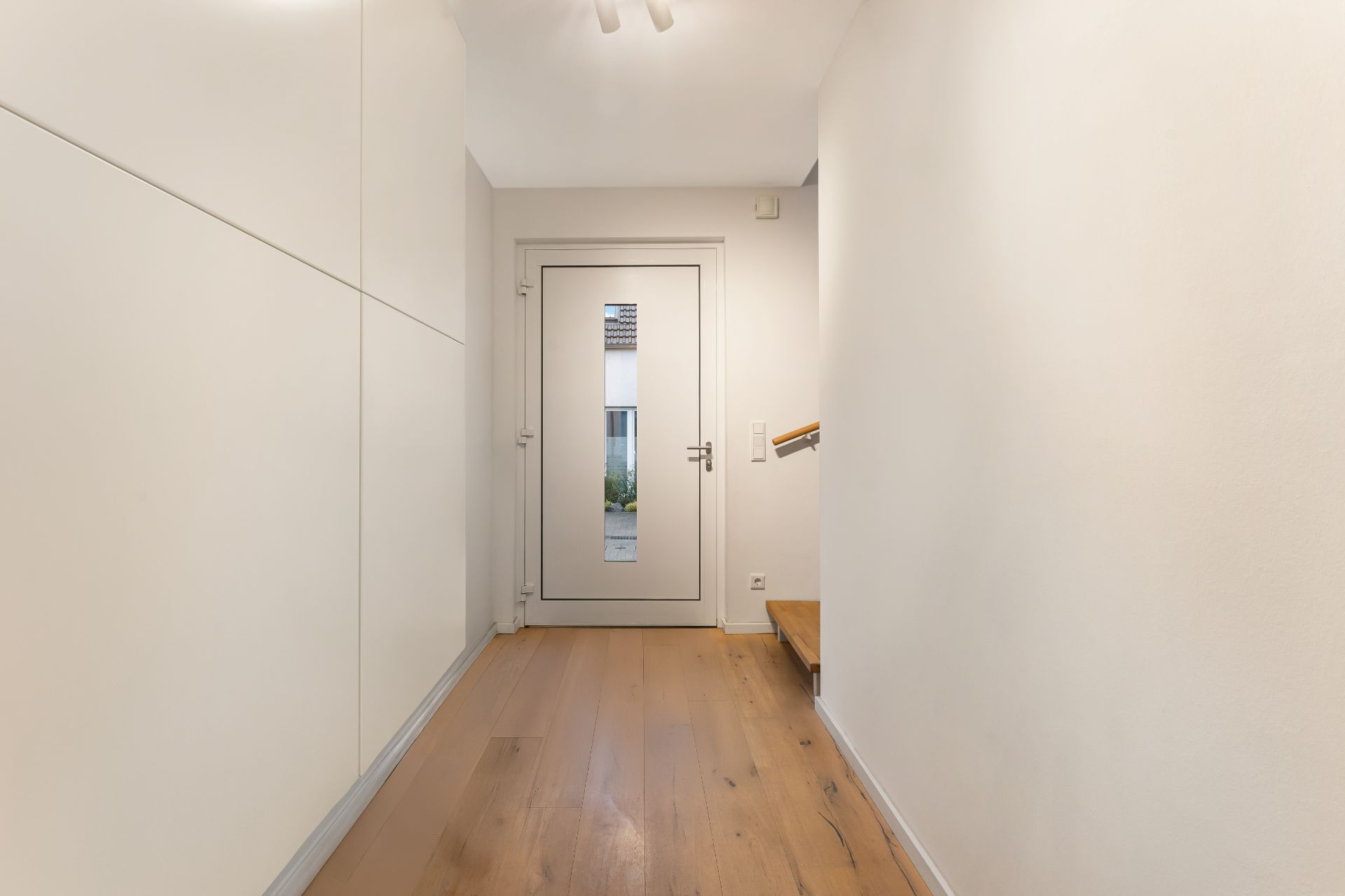 Heller Flur mit Holzboden, weißer Tür am Ende und Treppe an der rechten Seite.