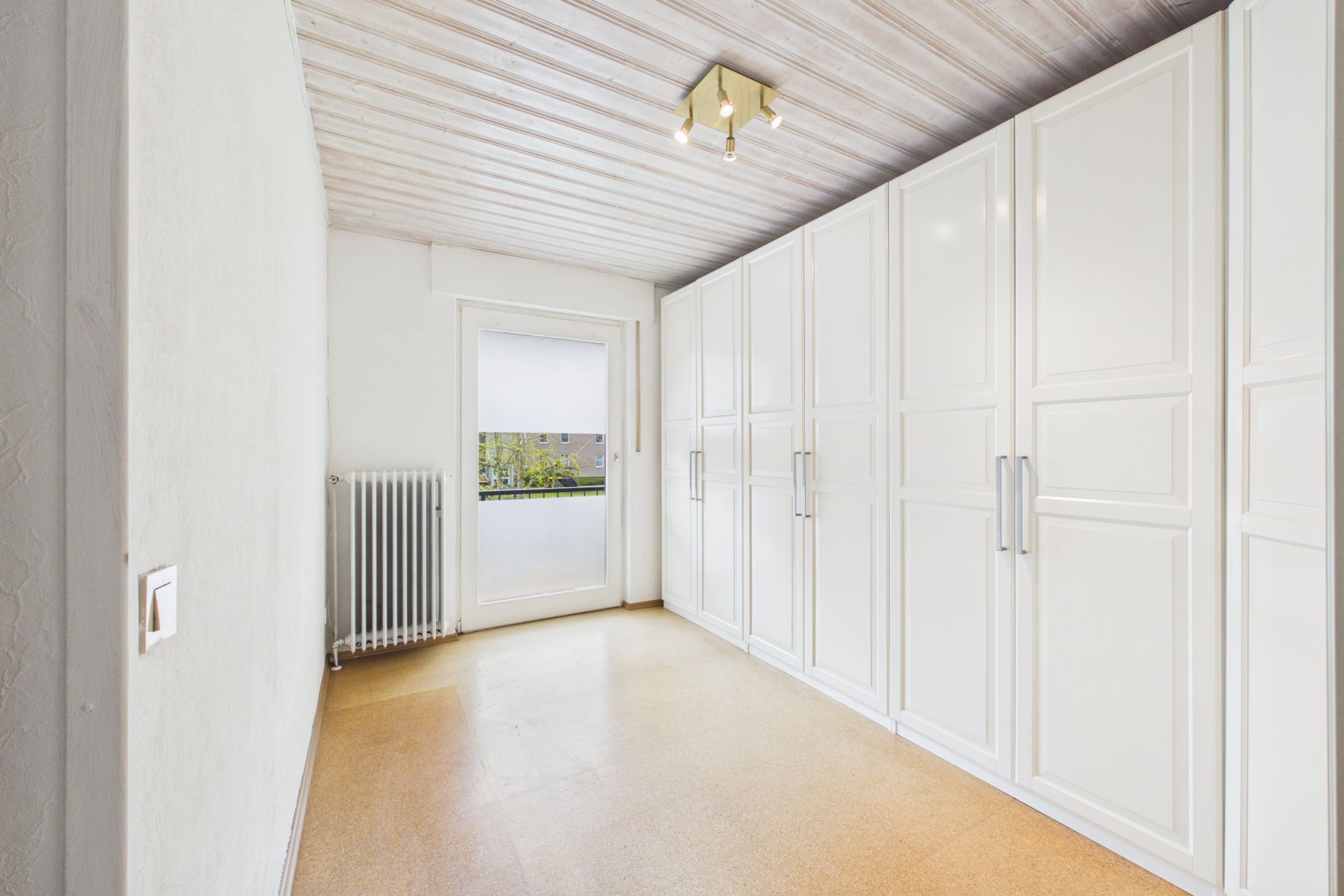 Heller Raum mit großer Fenster- und Türfront, weißen Einbauschränken und Deckenleuchte.