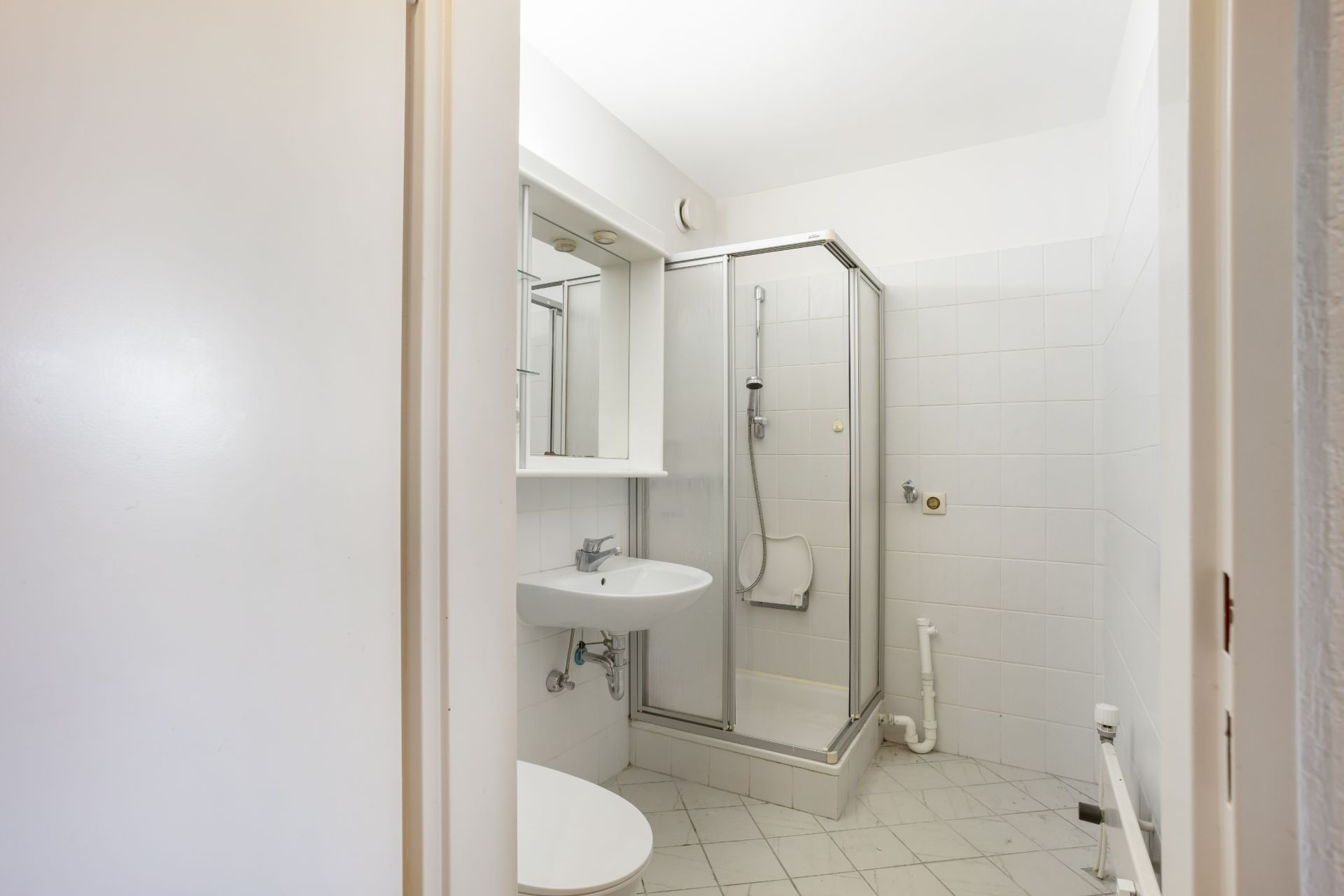 Helles Badezimmer mit Dusche, Waschbecken, Spiegel und weißen Fliesen.