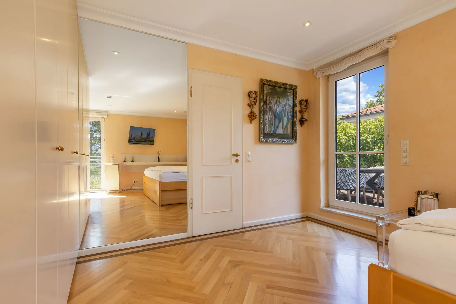 Helles Schlafzimmer mit Parkettboden, großem Spiegel, Fenster und Wandbild.