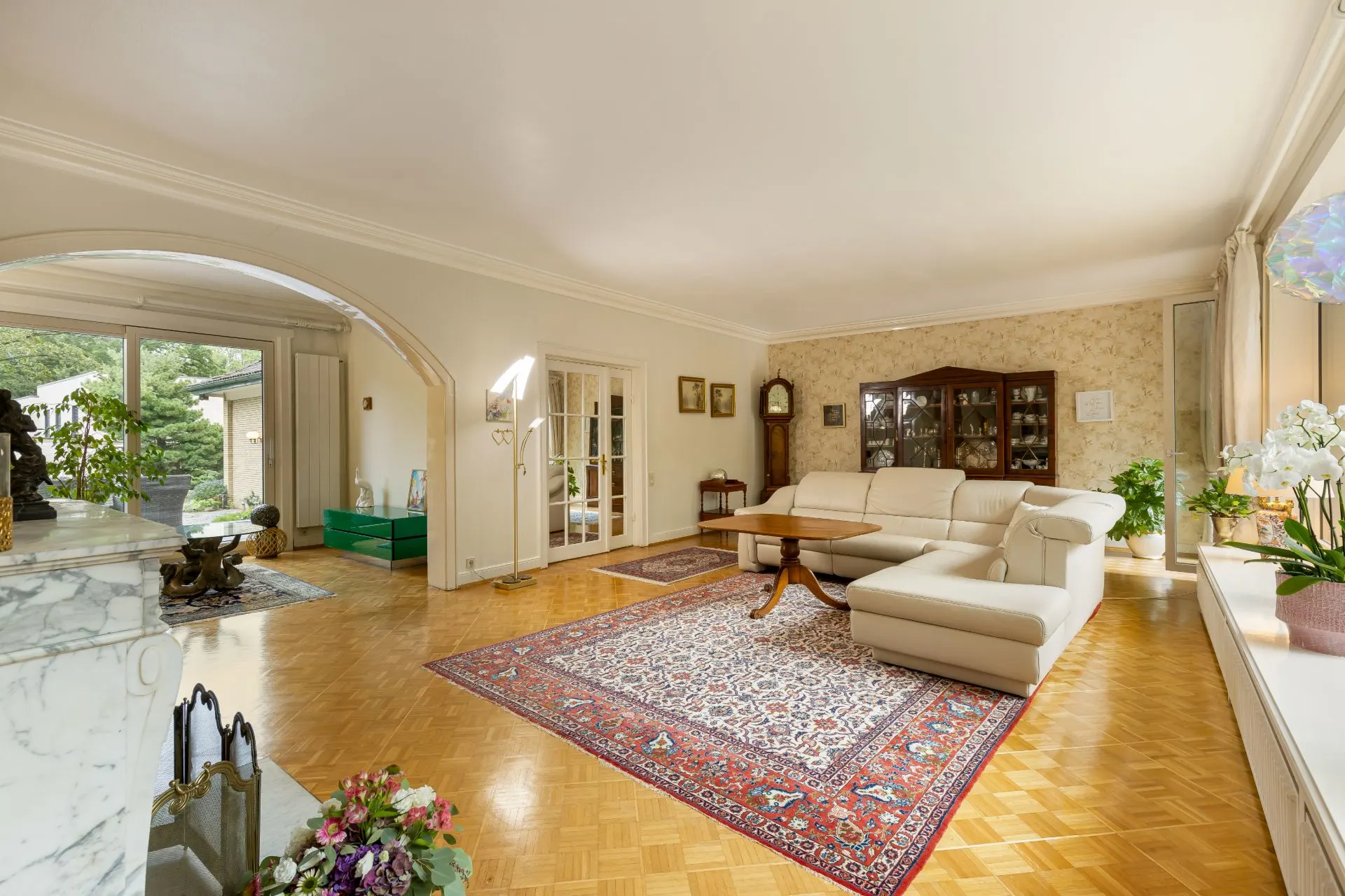 Helles Wohnzimmer mit Parkettboden, weißem Sofa, Teppich und großen Fenstern.