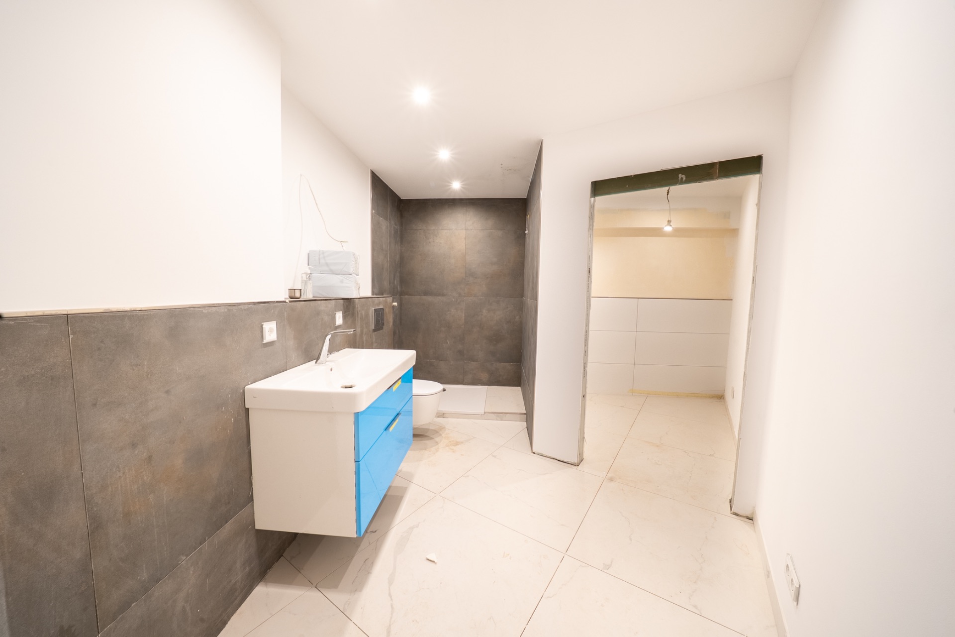 Modernes Badezimmer mit blauem Waschbecken, grauen Fliesen und offener Dusche.