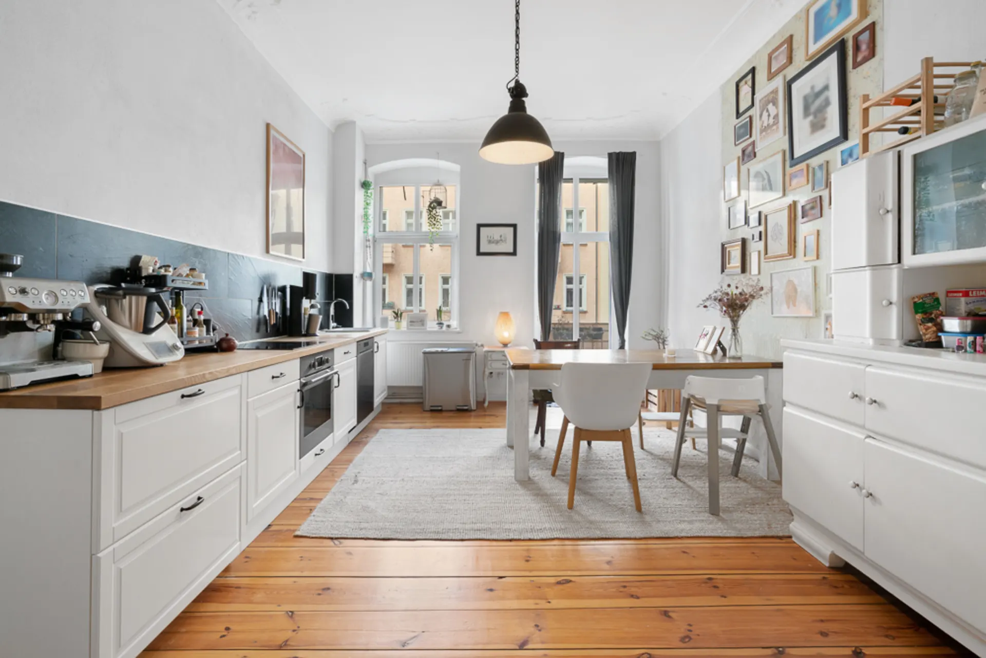 Helle Küche mit Esstisch, weißen Möbeln, Holzboden und vielen Bildern an der Wand.