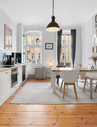 Helle Küche mit Esstisch, weißen Möbeln, Holzboden und vielen Bildern an der Wand.