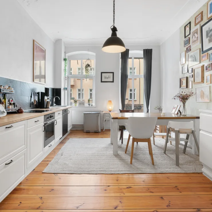 Helle Küche mit Esstisch, weißen Möbeln, Holzboden und vielen Bildern an der Wand.