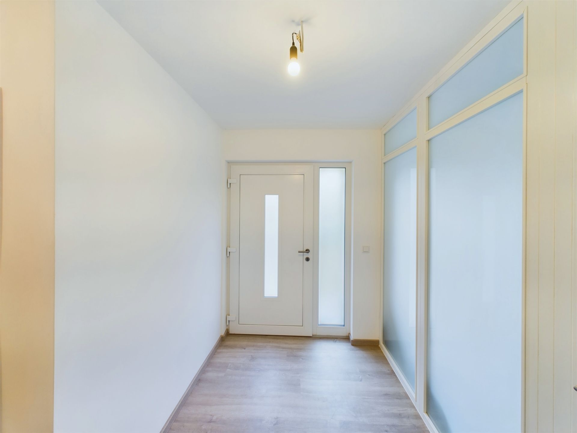 Heller Flur mit weißer Eingangstür, Holzboden und raumhohen Glaselementen an der Seite.