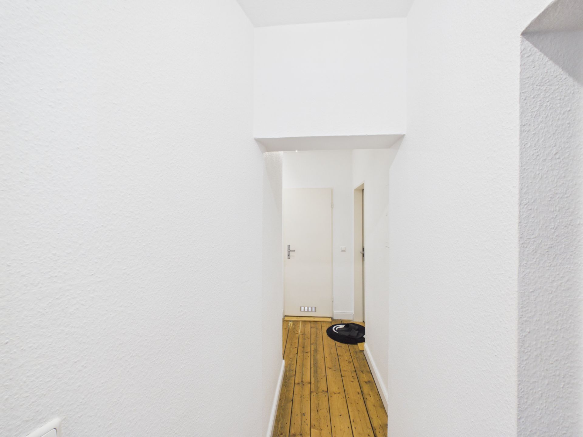 Heller Flur mit weiß gestrichenen Wänden und Holzboden, Tür am Ende.