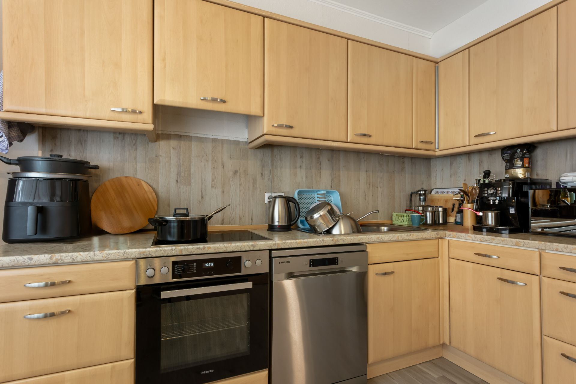 Moderne Küche mit Holzschränken, Spülmaschine, Herd und Küchengeräten auf der Arbeitsplatte.