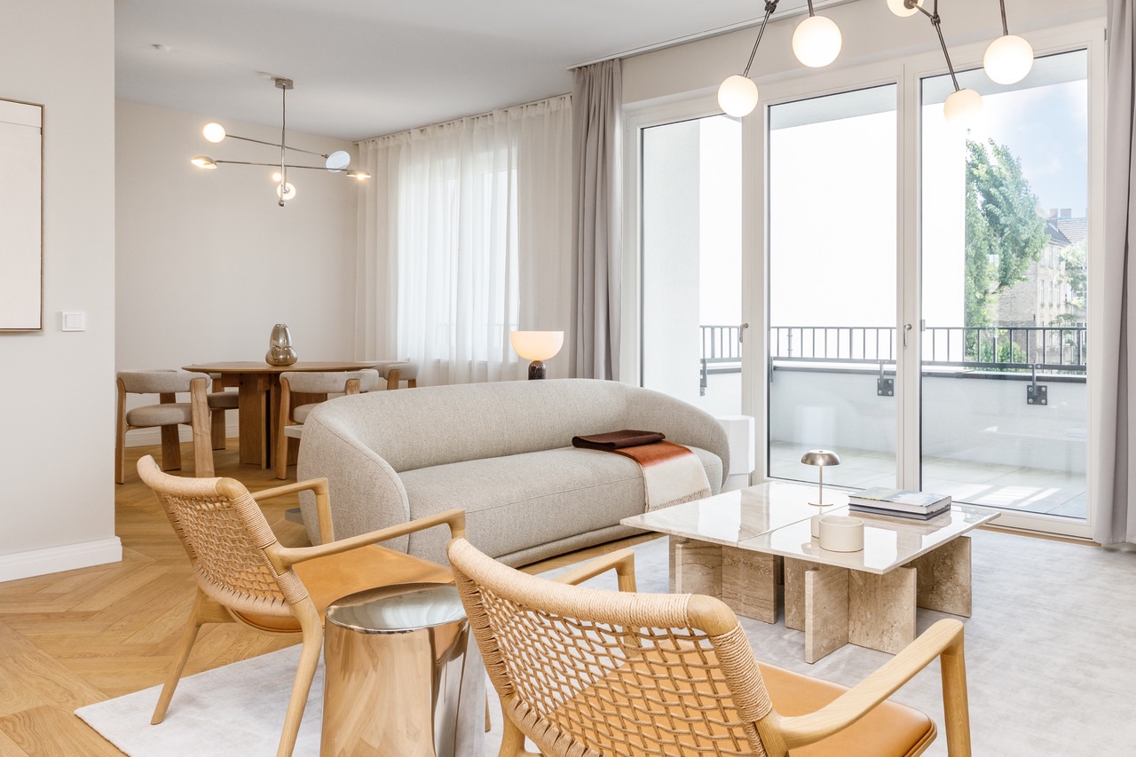 Modernes Wohnzimmer mit hellen Möbeln, Esstisch im Hintergrund und großen Fenstern zur Terrasse.