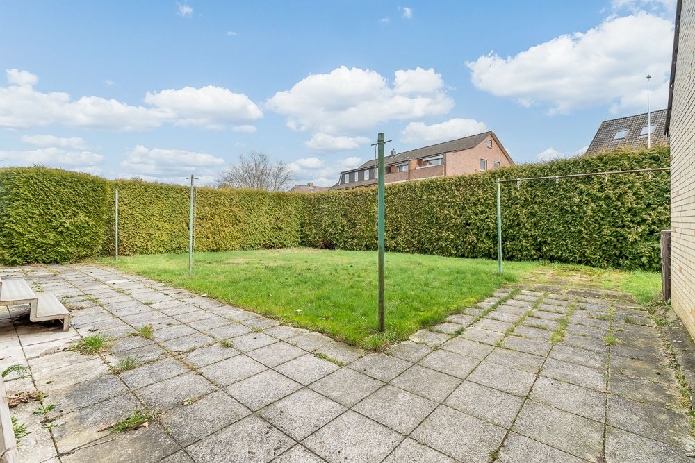 Garten mit Rasen, Wäscheleinen und gepflasterter Terrasse, von hohen Hecken umgeben.
