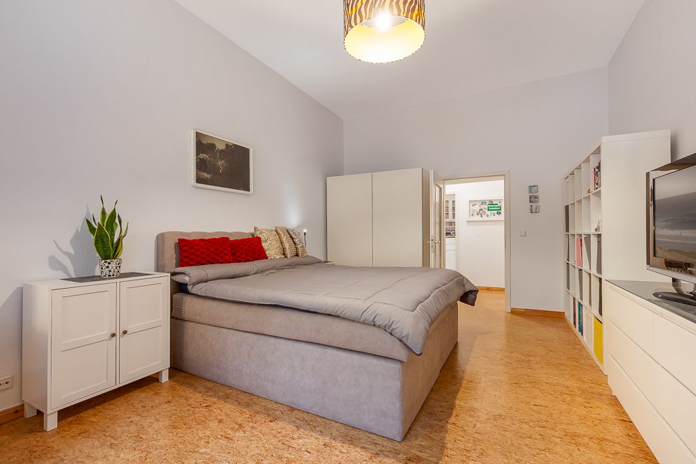 Geräumiges Schlafzimmer mit Doppelbett, weißen Schränken, Regalwand und Fernseher.