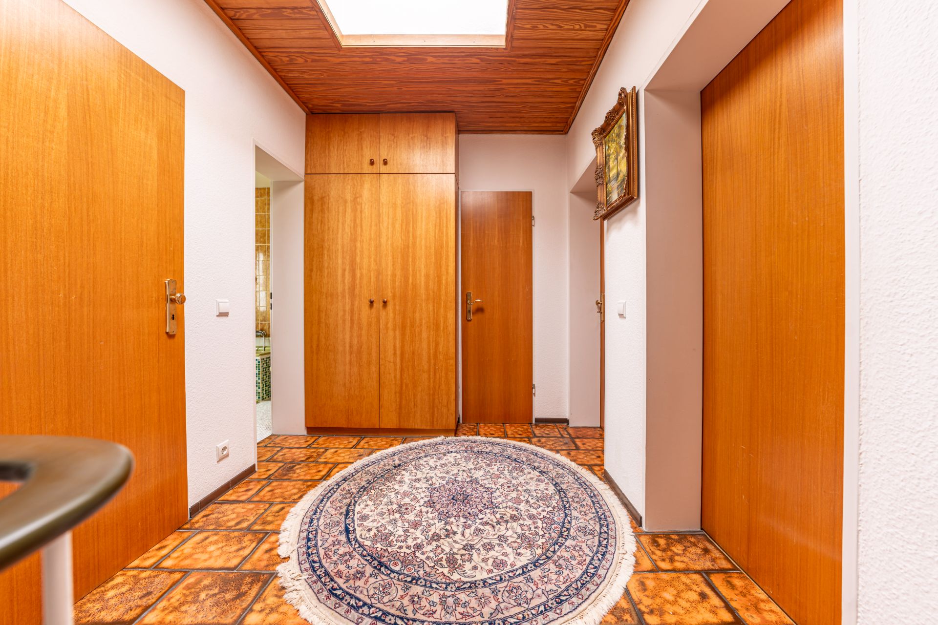Flur mit Holztüren, Einbauschrank, Teppich und gemusterten Fliesen.