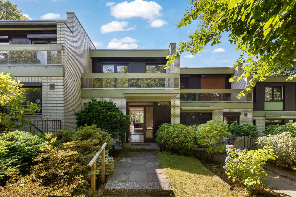 Moderne Wohnhausfassade mit großen Fenstern, Balkon und begrüntem Vorgarten.
