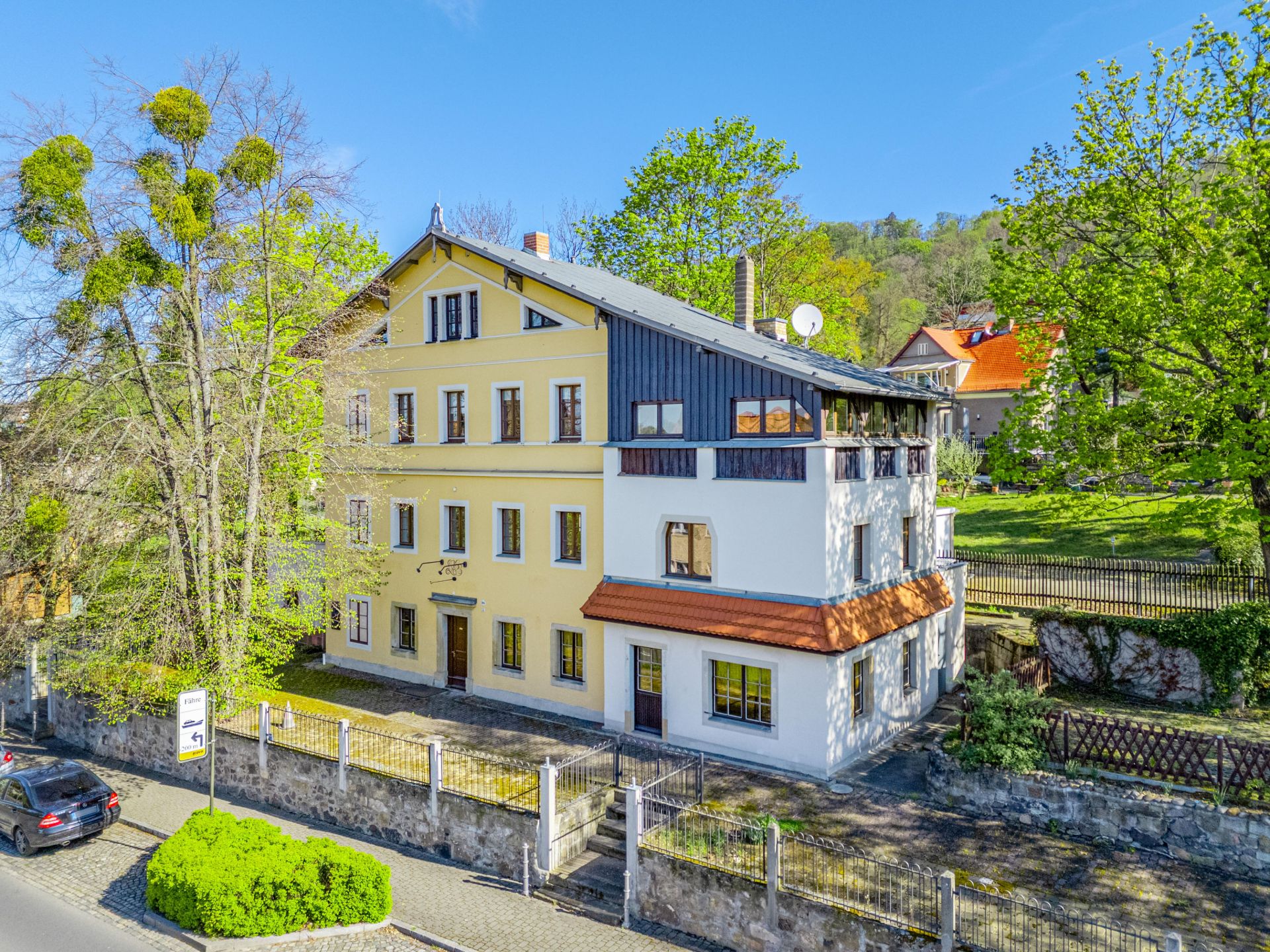 Großes, mehrstöckiges Wohnhaus mit gelber Fassade und umzäuntem Vorgarten.