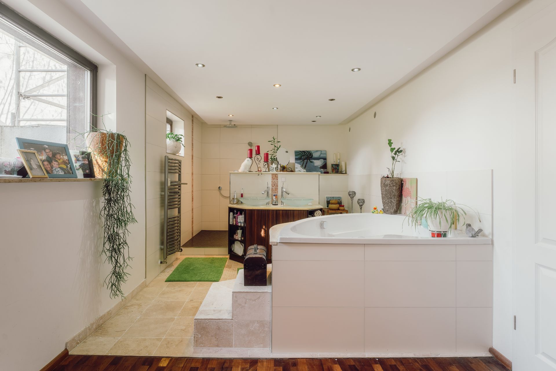 Modernes Badezimmer mit großer Badewanne, Doppelwaschbecken, Pflanzen und Fotos am Fenster.