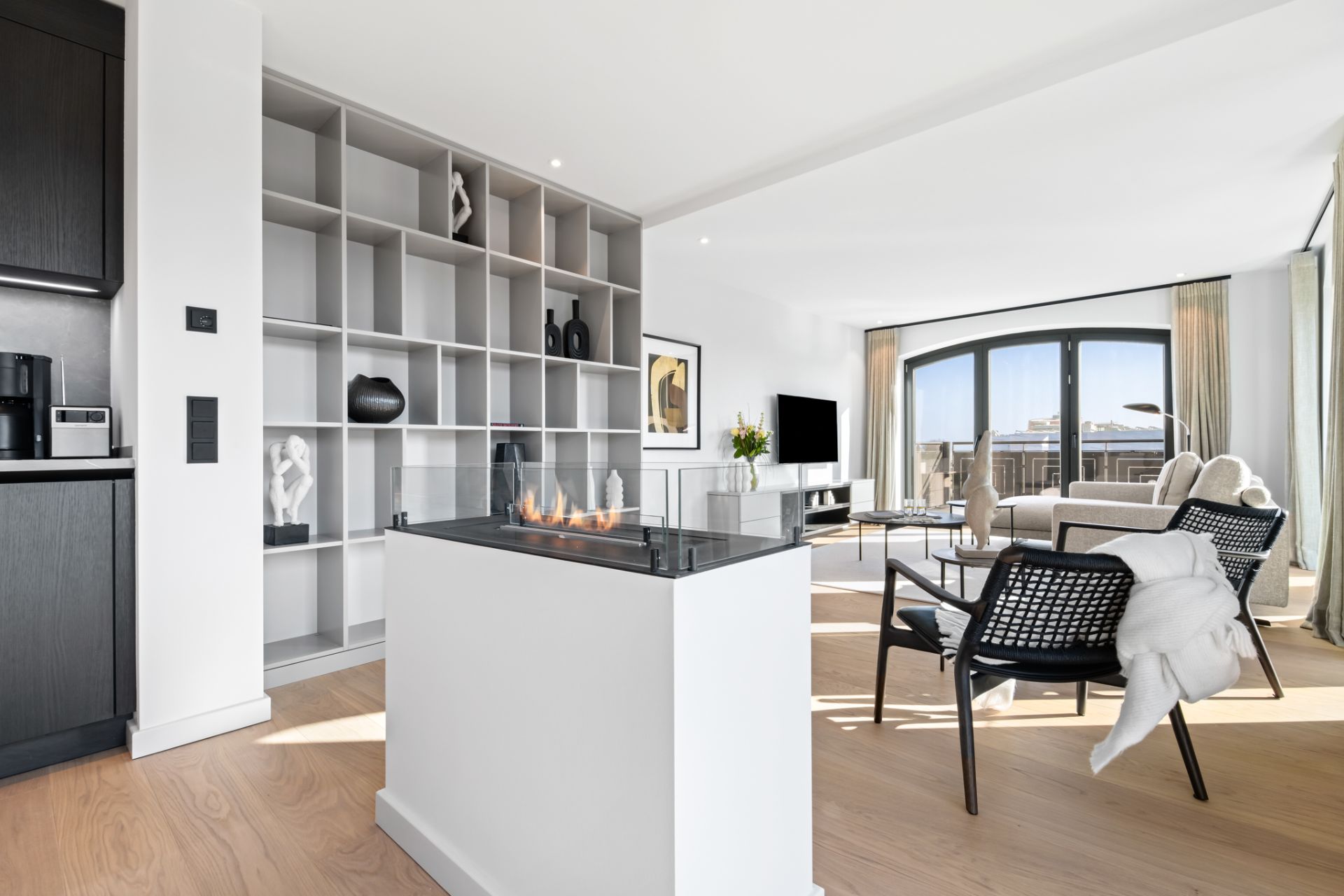 Modernes Wohnzimmer mit offenem Regal, Kamin, Sofa, Sesseln und großen Fenstern.