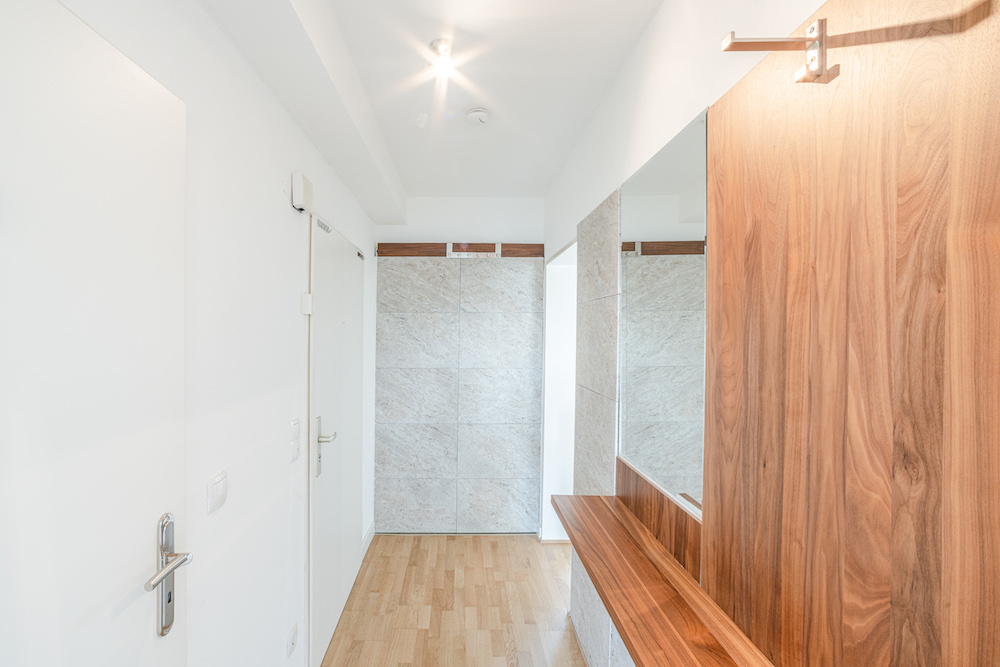 Heller Flur mit Holzboden, Spiegel und Holzgarderobe an der rechten Wand.