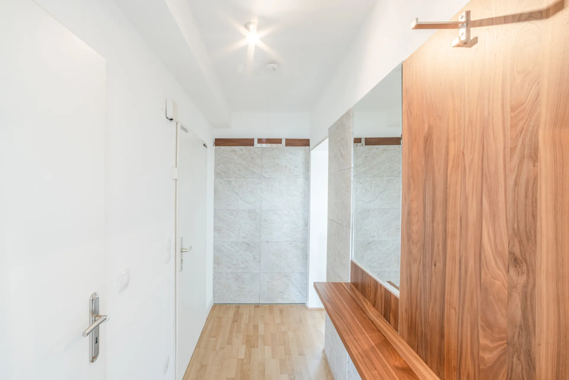 Heller Flur mit Holzboden, Spiegel und Holzgarderobe an der rechten Wand.