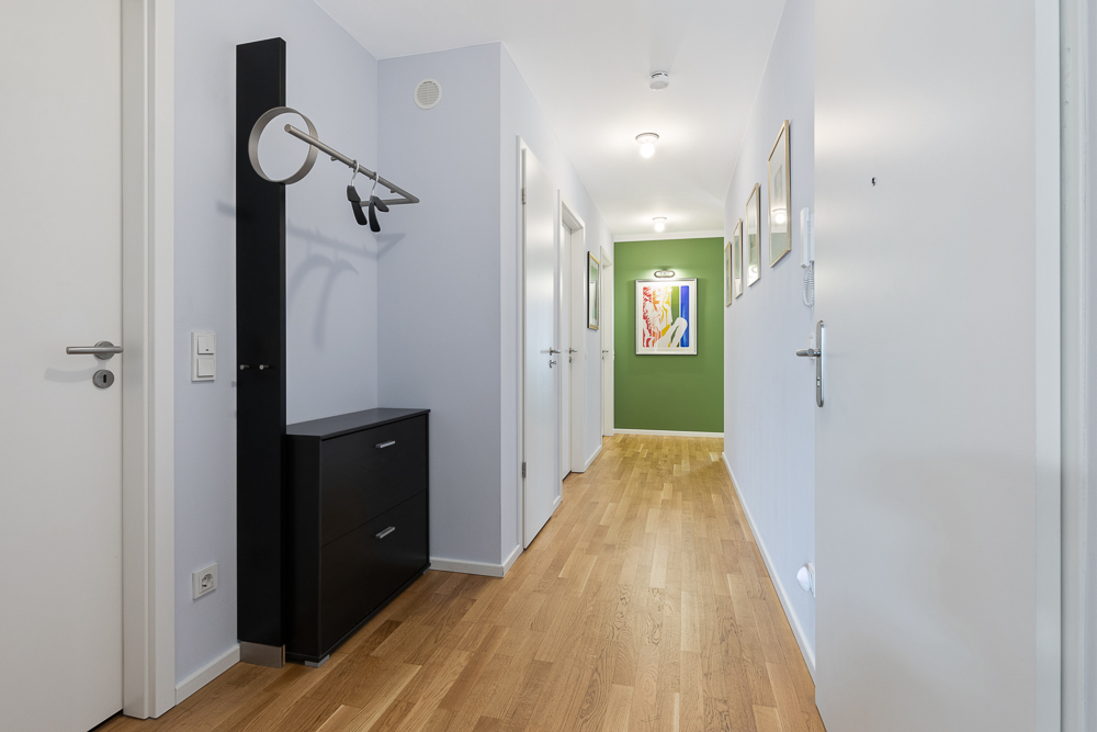 Heller Flur mit Holzboden, Garderobe, Kommode und Bildern an den Wänden.