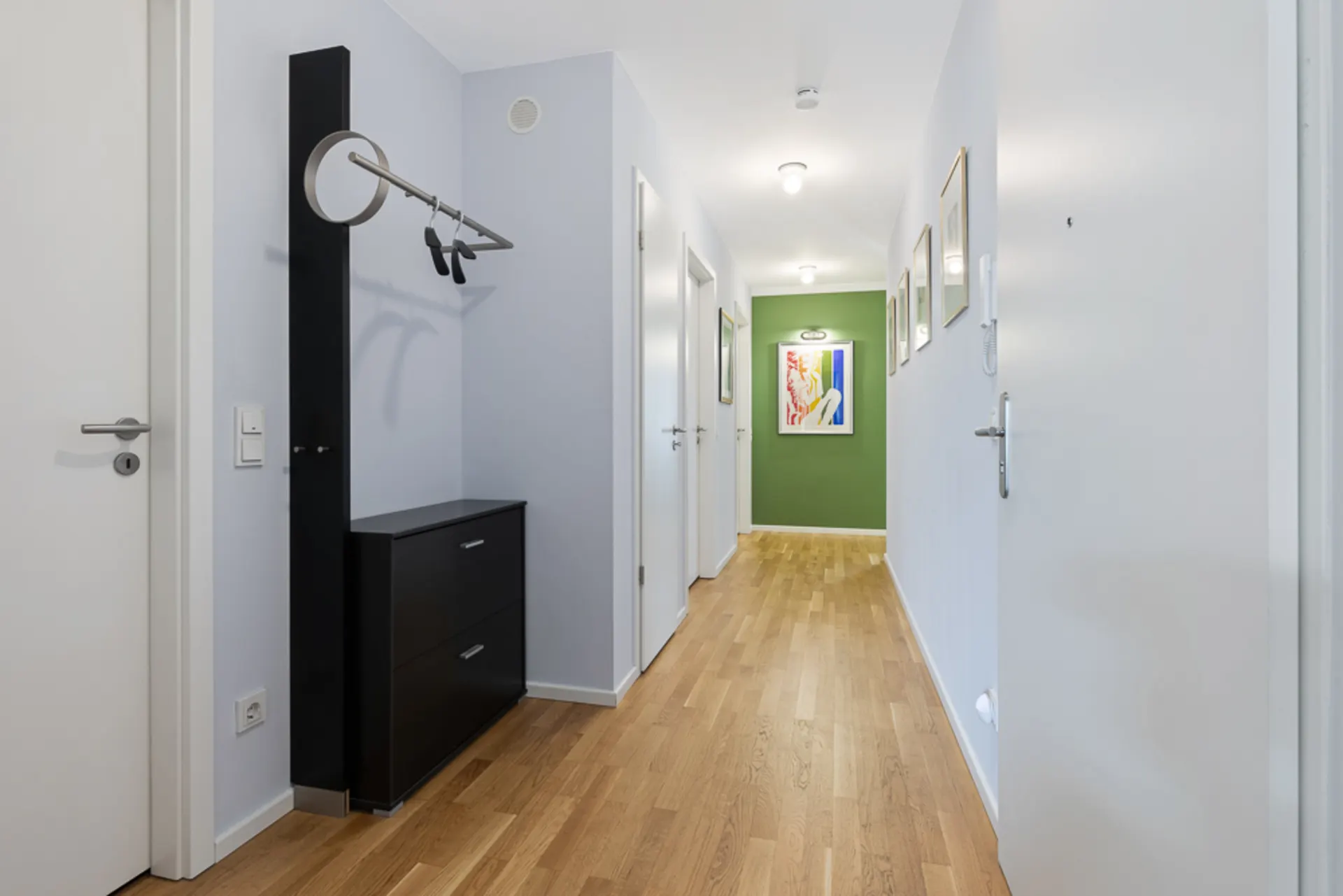 Heller Flur mit Holzboden, Garderobe, Kommode und Bildern an den Wänden.