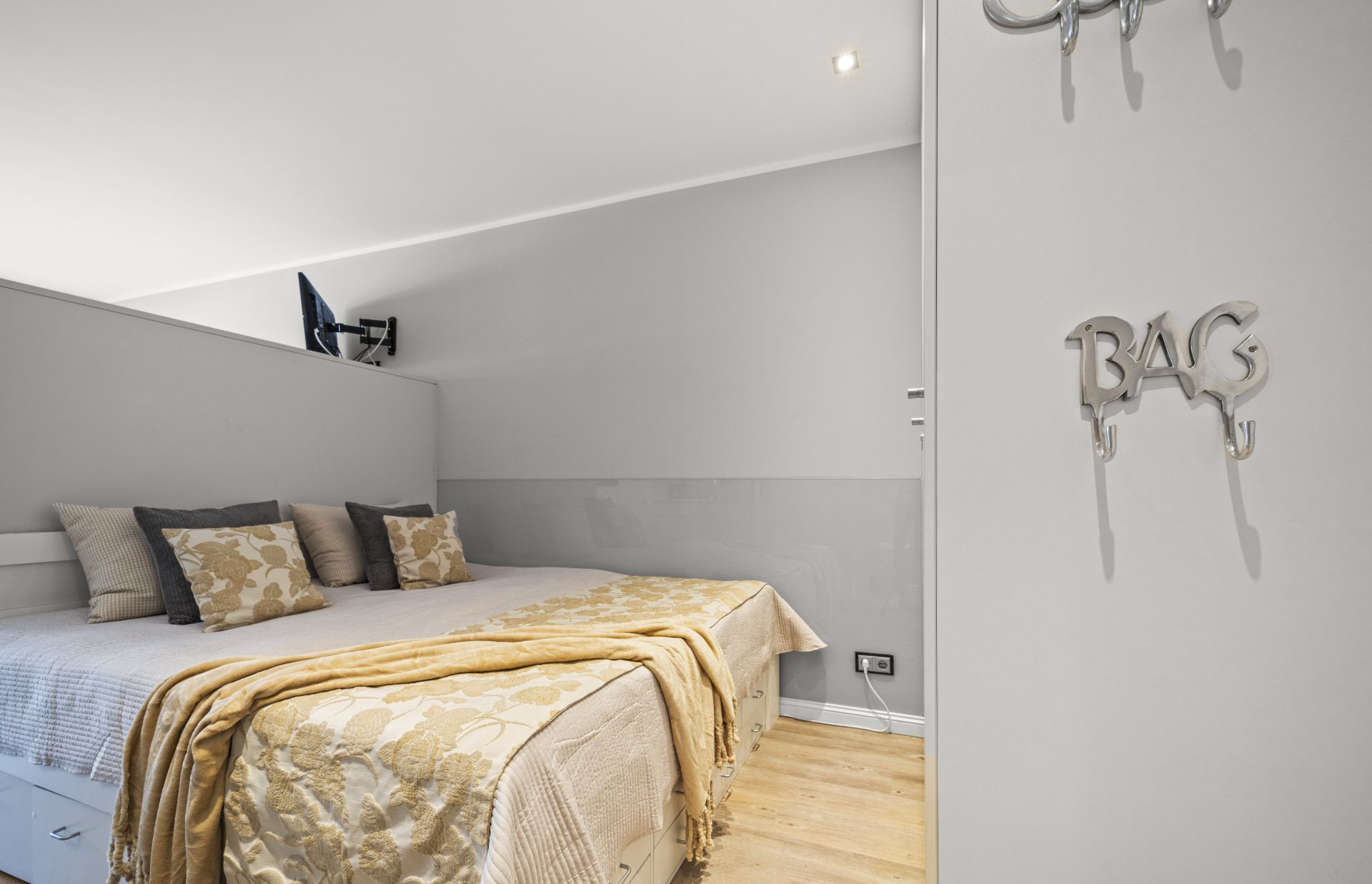 Helles Schlafzimmer mit Doppelbett, mehreren Kissen und Fernseher an der Wand.