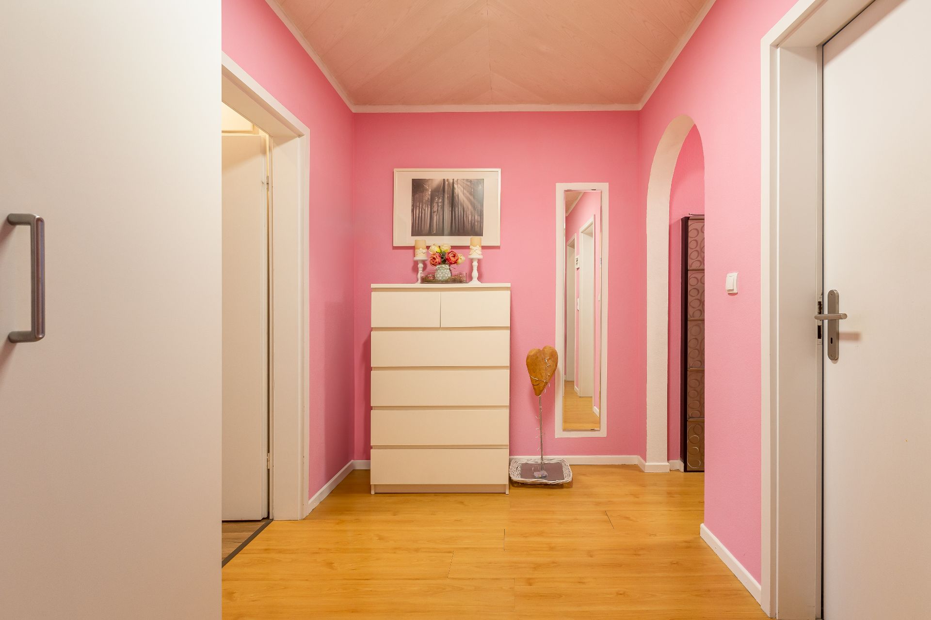 Flur mit rosa Wänden, Holzfußboden, weißer Kommode und Wandspiegel.
