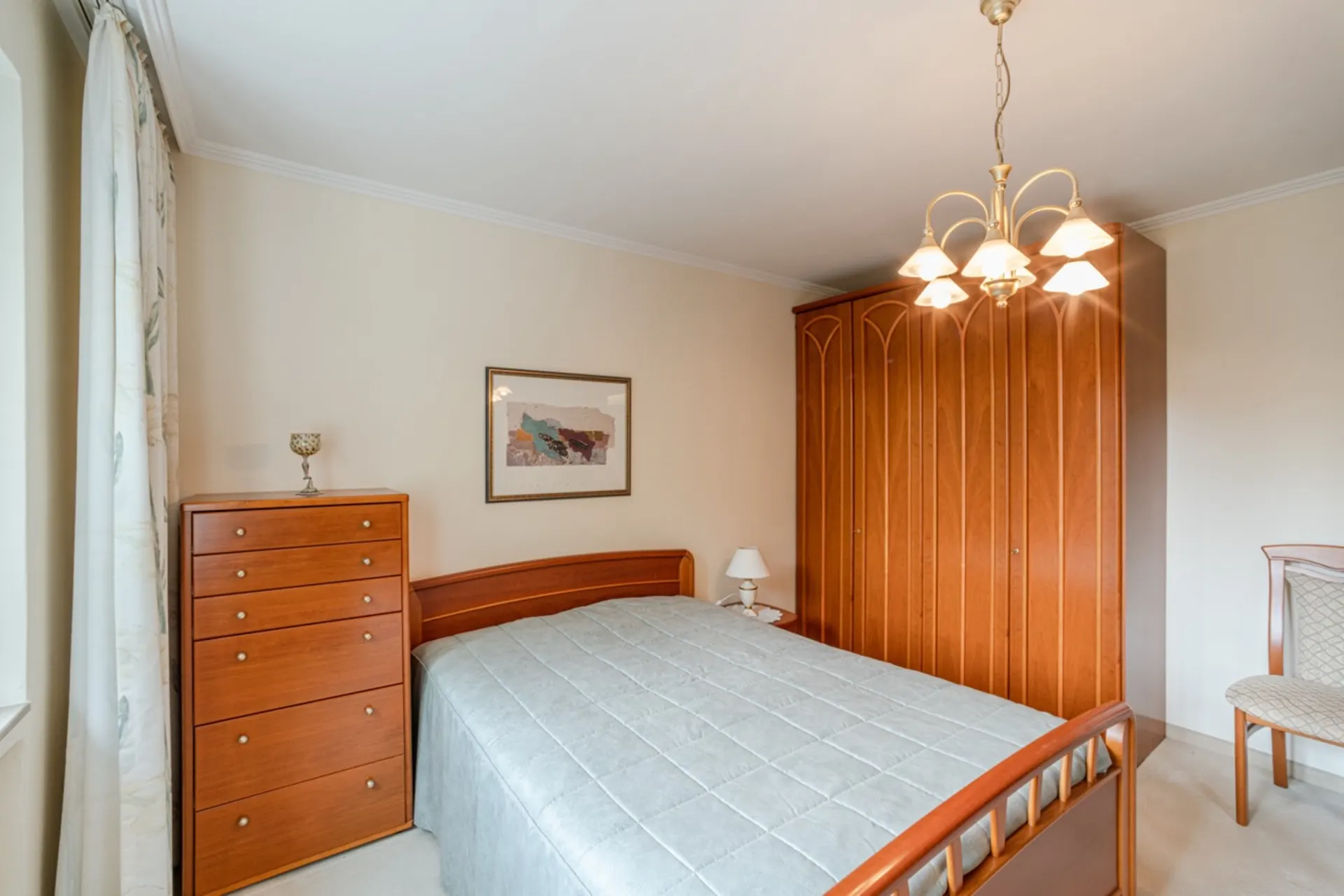 Helles Schlafzimmer mit Holzbett, Kommode, Kleiderschrank und Deckenlampe.