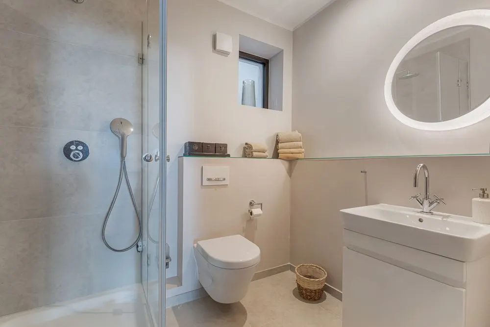 Modernes Badezimmer mit Dusche, WC, Waschbecken, beleuchtetem Spiegel und Handtüchern.