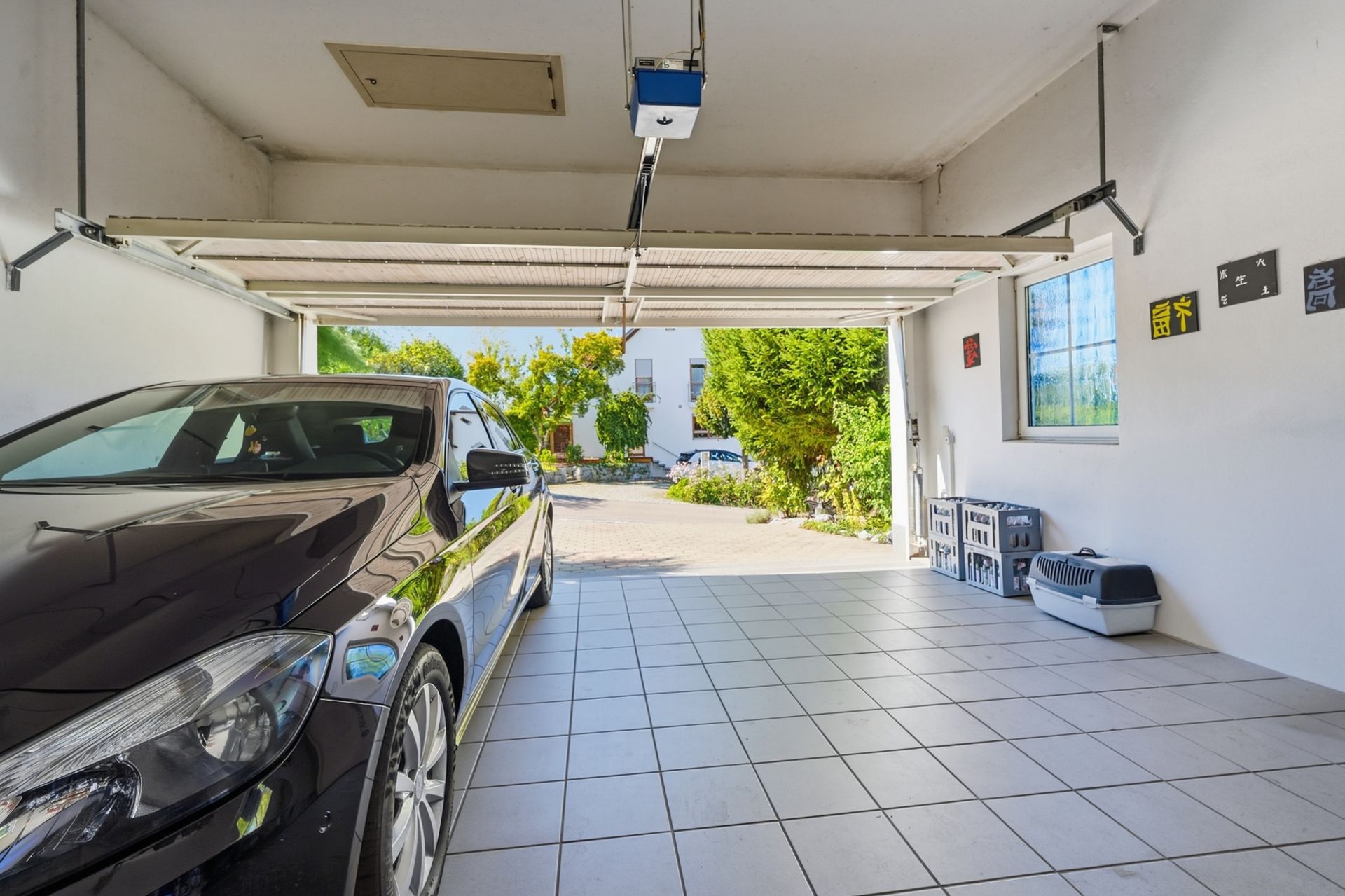 Offene Garage mit geparktem Auto, Fliesenboden und Blick auf Einfahrt sowie Garten.