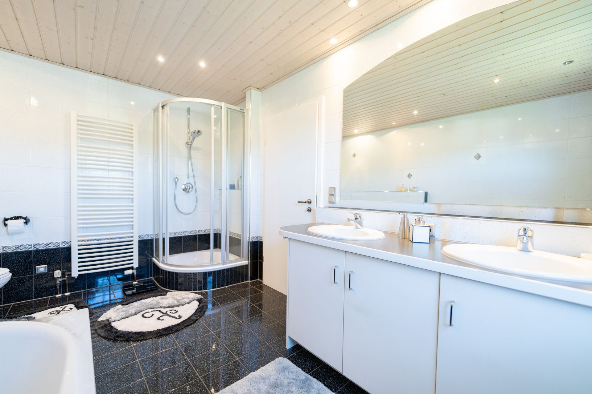 Modernes Badezimmer mit Dusche, Doppelwaschbecken, großem Spiegel und dunklem Fliesenboden.